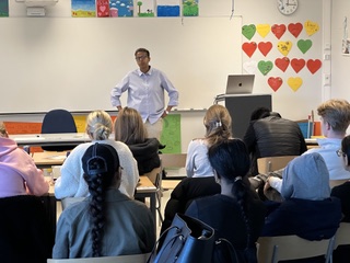 Foredragsholder snakker til en klasse i et klasserom med tegninger på veggen.
